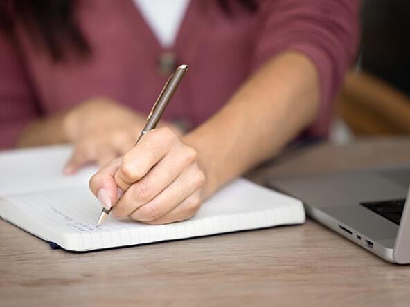 researcher taking notes in notebook next to laptop